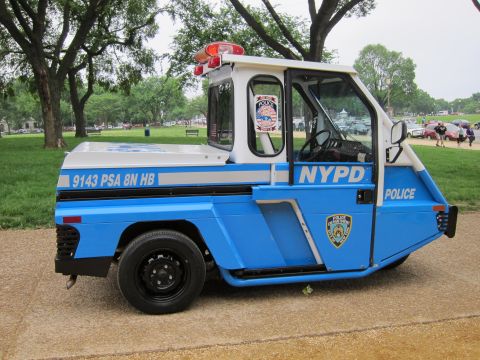 1991 Ford LTD Crown Victoria - Side profile of a compact blue-and-white NYPD three-wheeled scooter lettered 9143 PSA 8N HB in a grassy park.