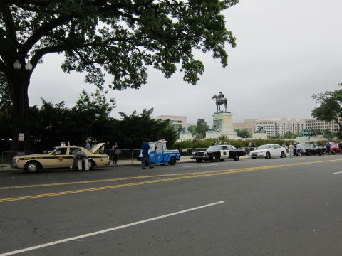 1991 Ford LTD Crown Victoria - lineup of vintage and modern police vehicles parked along a roadside near a domed building and an equestrian statue.