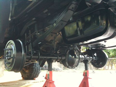 1996 Ford Bronco - The underside of a vehicle is shown, the rear axle, leaf springs, and drum brakes, all resting on red jack stands.