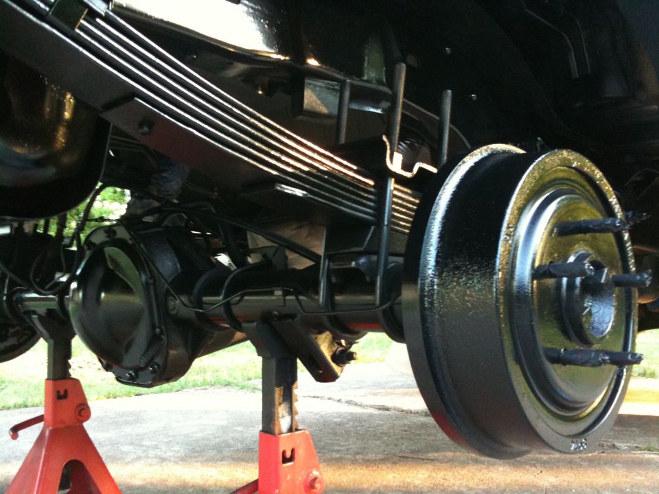 Rear axle assembly with leaf springs and brake drum, vehicle supported by red jack stands