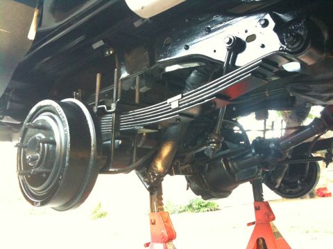 1996 Ford Bronco - Underside view of a vehicle's rear axle and suspension system, supported by red jack stands.