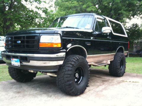1996 Ford Bronco - This lifted Ford Bronco is parked on a concrete driveway with trees in the background.