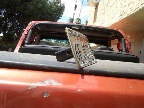 1978 Ford Bronco - The rear of an orange SUV is visible, with a California license plate placed on its tailgate.