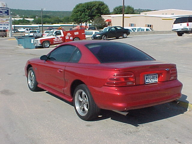 Red Ford Mustang coupe viewed from rear three-quarter in a parking lot
