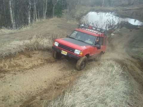 1990 Chevrolet Suburban - A red Land Rover Discovery 1 navigates a challenging muddy off-road course.