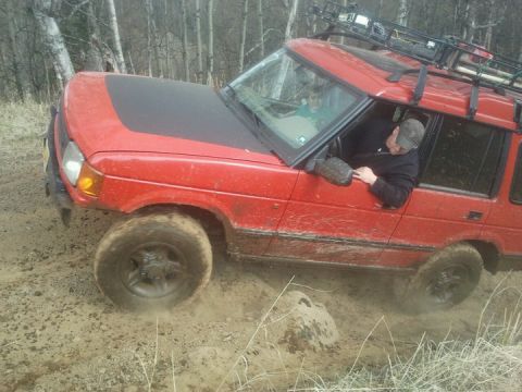 1990 Chevrolet Suburban - This red SUV, equipped with a roof rack, navigates a muddy off-road trail.