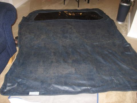 1990 Ford Bronco - A dark blue car cover, possibly for a convertible, is laid out on the floor next to a couch.