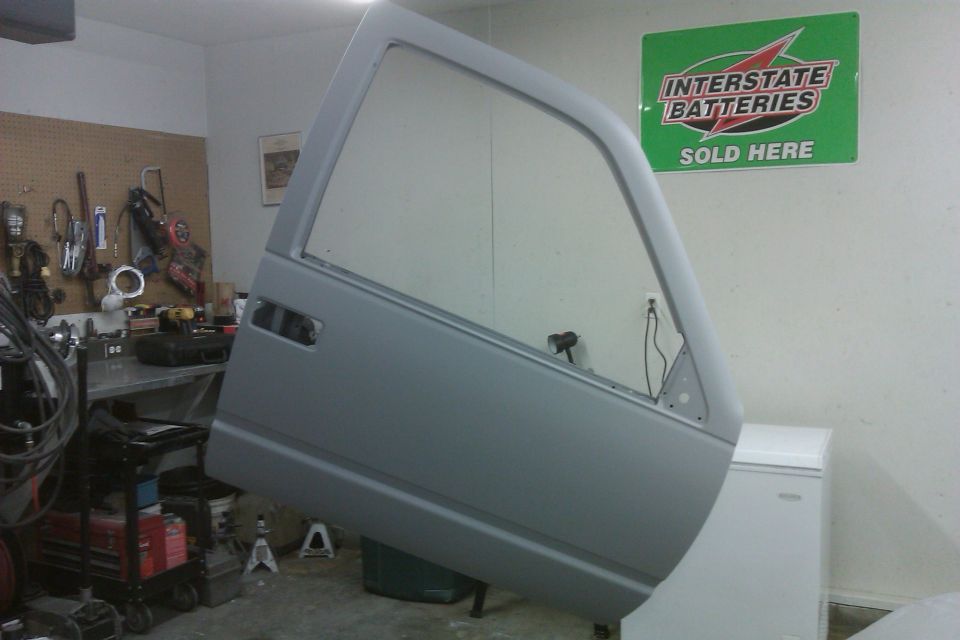 Gray vehicle door hanging in a garage, tools on wall behind it, Interstate Batteries sign on wall