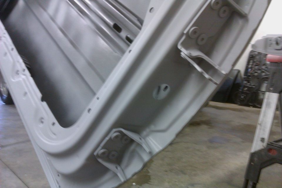 Interior view of a car door frame, showing hinges and mounting points. The metal is painted gray