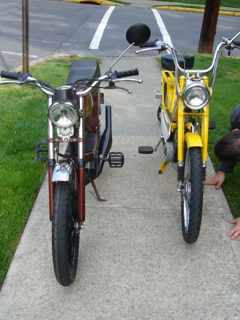 1981 Garelli Rally Sport - Two mopeds, a brown one and a yellow one, are parked side-by-side on a concrete path next to a grassy area.