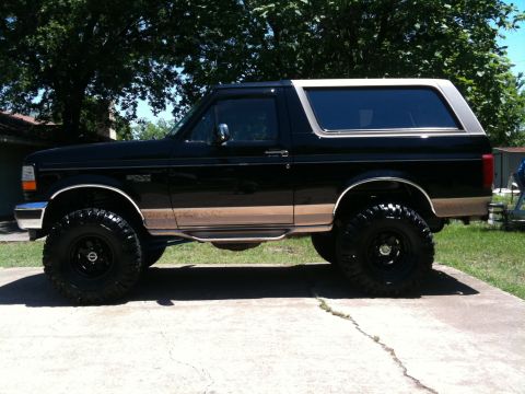 1996 Ford Bronco - Side view of a lifted black Ford Bronco with tan accents and large off-road tires.