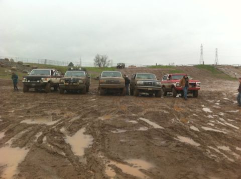 1990 Ford Bronco - Several SUVs, including a 1990 Ford Bronco, are parked in a muddy off-road area.