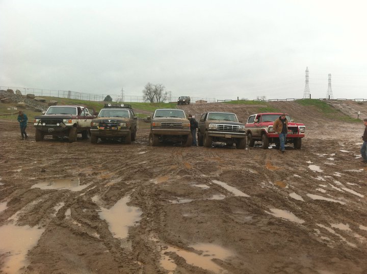 Five SUVs lined up in mud, front view. One is a 1990 Ford Bronco