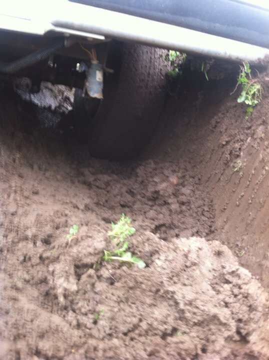 Vehicle undercarriage stuck in mud, showing tire and wiring