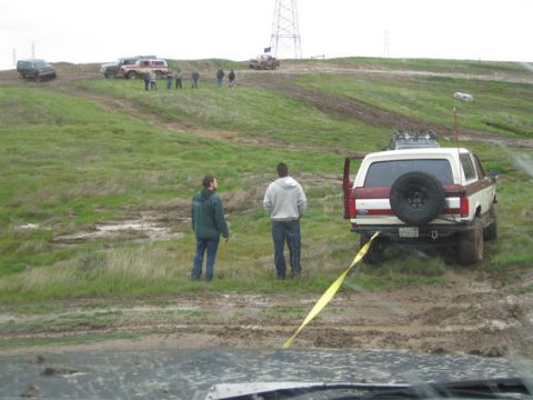 1990 Ford Bronco - A group of people and several off-road vehicles are gathered on a muddy, grassy hill.