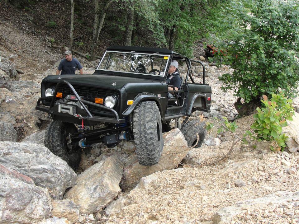 Black Ford Bronco with off-road modifications navigating a rocky trail. Driver and passenger are visible