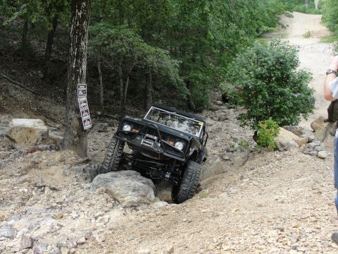 1967 Ford Mustang - A black off-road vehicle tackles a challenging rocky terrain on a wooded trail.