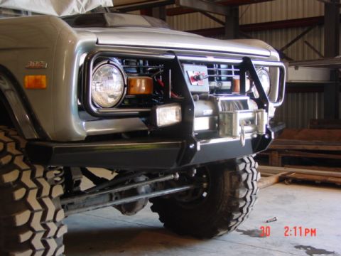 1978 Ford Bronco - Low front-end view of a lifted tan and silver 4x4 fitted with a heavy black winch bumper, tubular brush guard hoops and a Warn winch, plus…