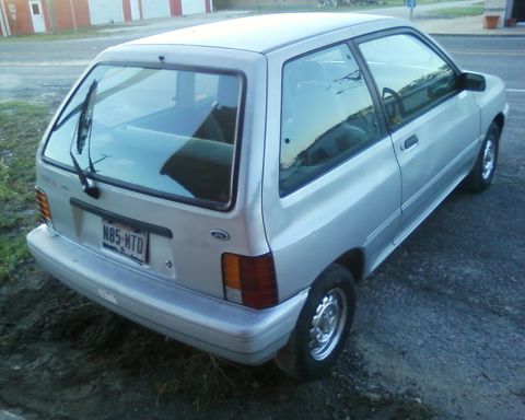 1991 Ford Festiva - Silver 1991 Ford Festiva hatchback seen from the rear 3/4 angle on a gravel surface.