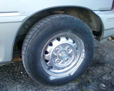 1991 Ford Festiva - Close-up of a rear wheel on a silver vehicle, a chrome rim with a blue Ford logo.
