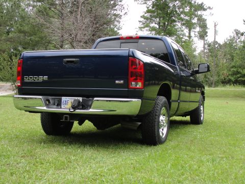 1967 Ford Mustang - Rear view of a dark blue Dodge Ram pickup truck parked on a grassy area with trees in the background.