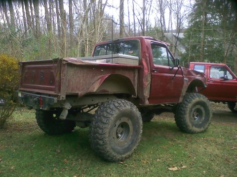 1988 Ford Bronco - Modified red Ford pickup truck with oversized tires and a toolbox in the bed.