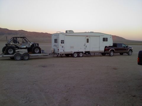 2011 Ford F-250 - A dark brown 2011 Ford F-250 tows a large RV and a trailer carrying a buggy in a desert landscape.