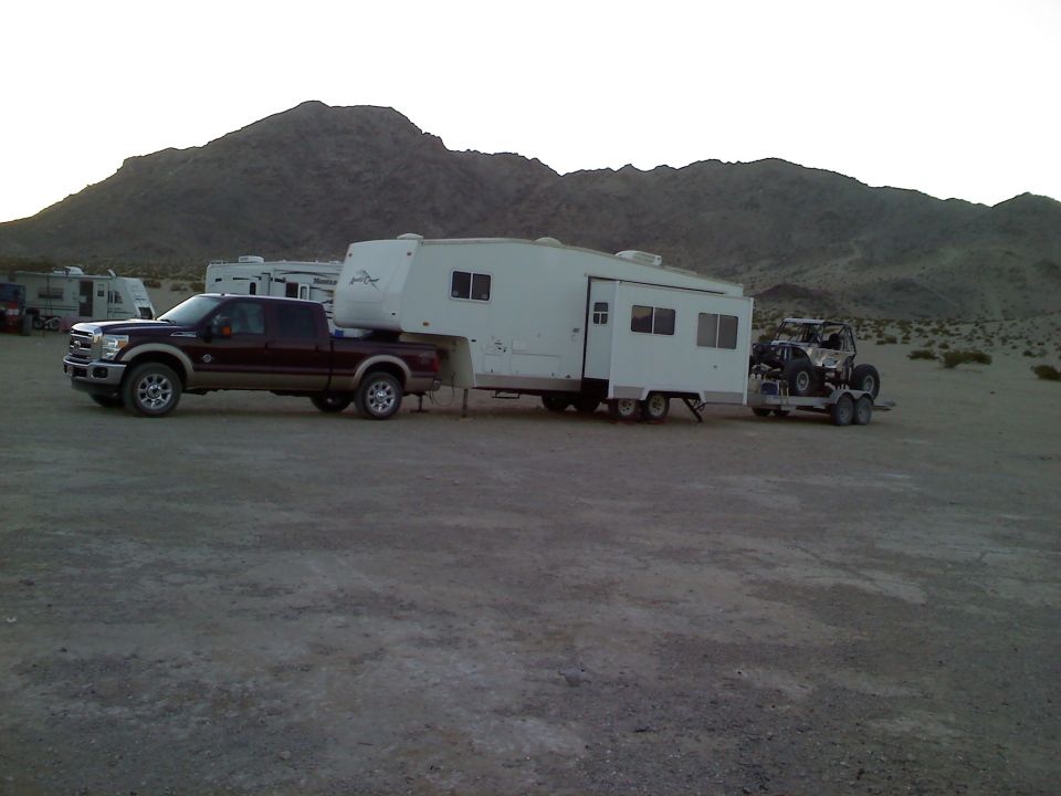 Ford F-250 towing a fifth-wheel trailer with a UTV on a trailer behind it in a desert landscape