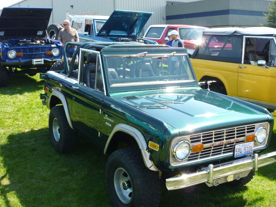 Green 1975 Ford Bronco parked on grass, other Broncos visible behind it
