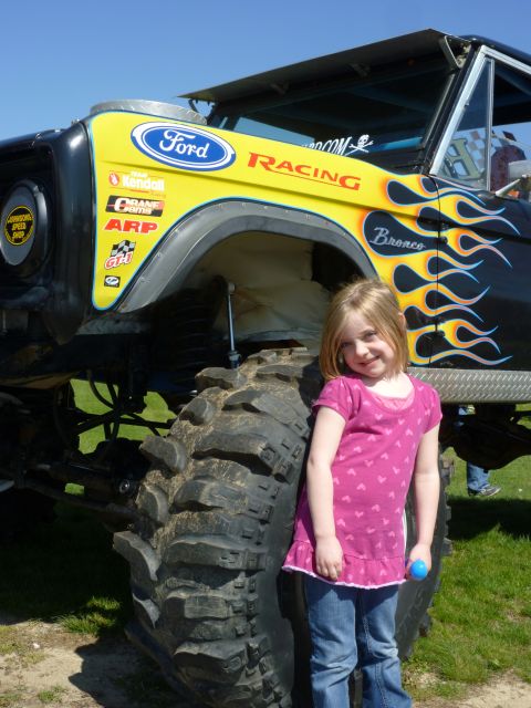 1995 Ford Bronco - Modified 1995 Ford Bronco features racing decals and flame graphics, with a young girl posing beside its large tire.