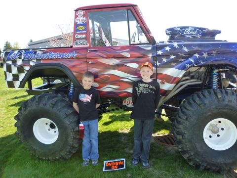 1995 Ford Bronco - A custom monster truck features patriotic paint and flames, with two children posing in front of it.