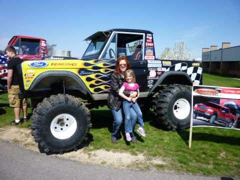 1995 Ford Bronco - A modified Ford Bronco, adorned with racing decals and flame graphics, is displayed with two people posing in front of it.