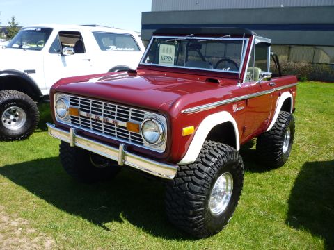 1995 Ford Bronco - Red 1975 Ford Bronco with lifted suspension and off-road tires is parked next to another Bronco.