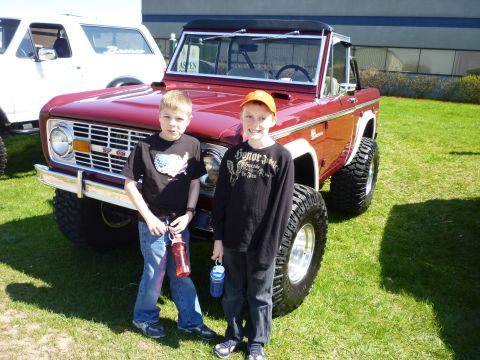 1995 Ford Bronco - A lifted red Ford Bronco is shown with two young boys posing in front of it at an outdoor event.