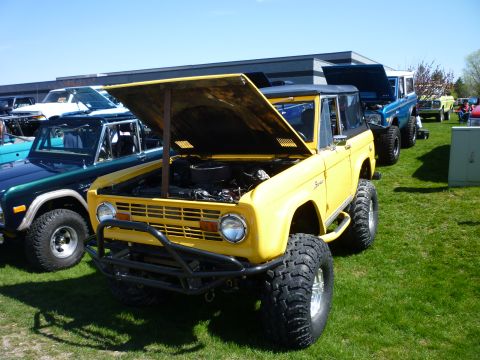 1995 Ford Bronco - Yellow Ford Bronco with aftermarket bumper and lifted suspension at an outdoor car show.