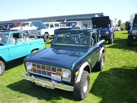 1995 Ford Bronco - A lineup of classic Ford Broncos are displayed on a grassy field under a clear sky.