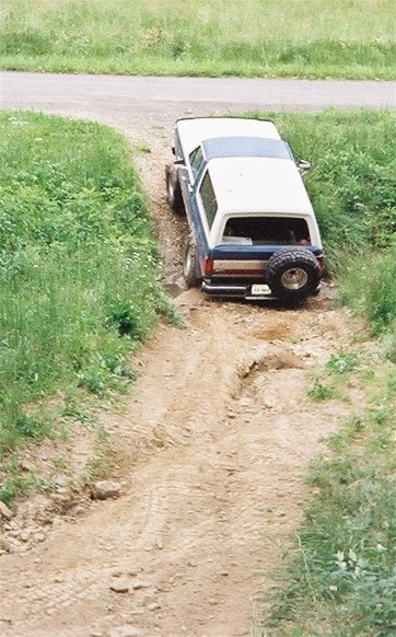1990 Ford Bronco - A Ford Bronco navigates a rough dirt track, its rear tire mounted externally.
