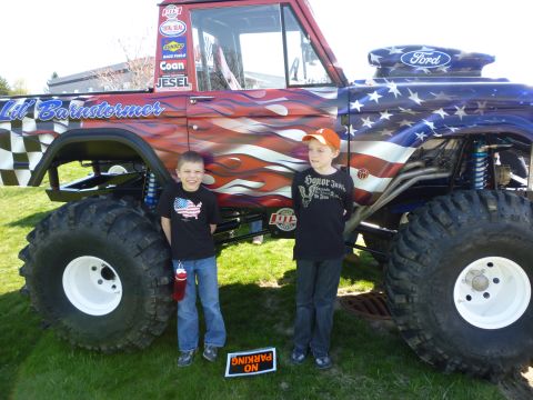 1995 Ford Bronco - Custom monster truck with patriotic paint scheme and two young boys posing beside it.