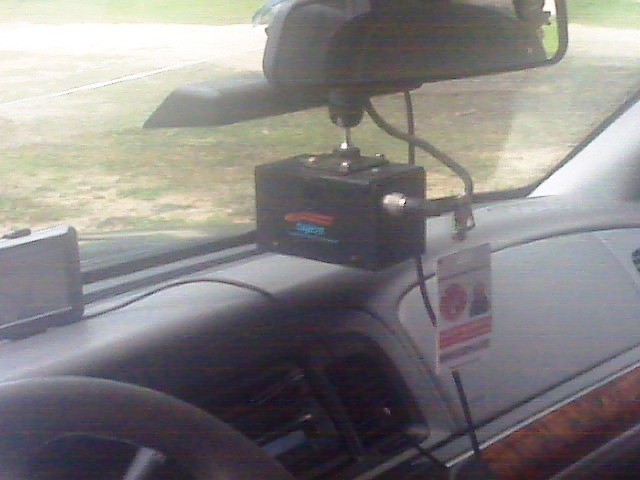 Dashboard interior with black electronic box mounted under rearview mirror and a hanging tag on the dash