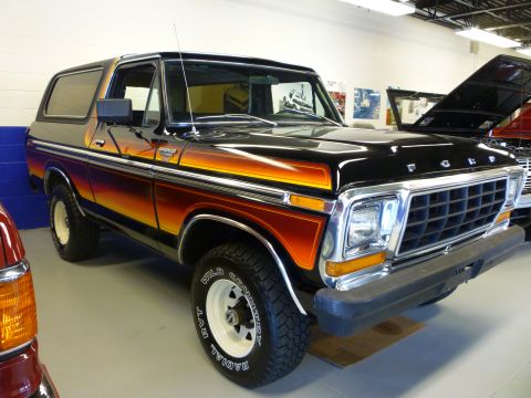 1995 Ford Bronco - This black Ford Bronco features a distinctive orange and yellow gradient stripe along its side. The vehicle is shown in a three-quarter fro…