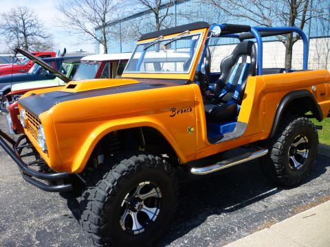 1995 Ford Bronco - This modified Ford Bronco features a bright orange exterior, black hood, and a prominent blue roll cage. The interior has racing seats and…