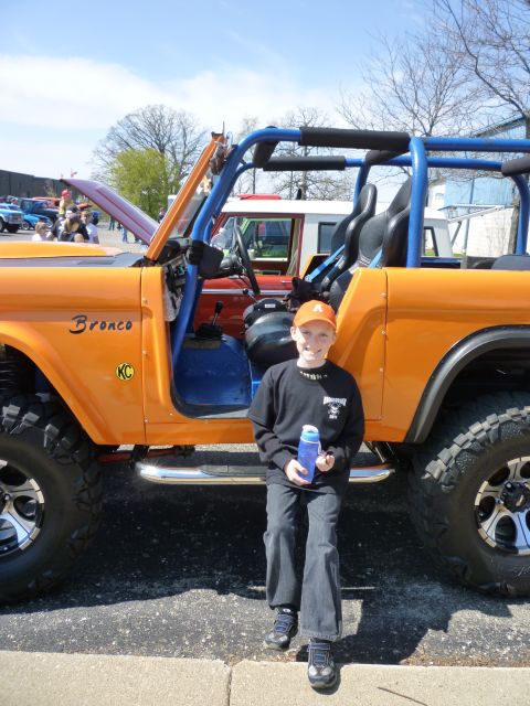 1995 Ford Bronco - A boy poses next to an orange Ford Bronco at an outdoor event. Another Bronco is visible in the background.