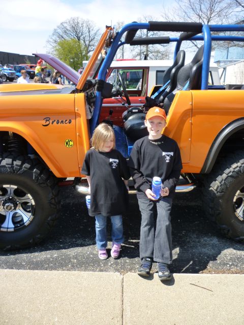 1995 Ford Bronco - This modified Ford Bronco features a bright orange exterior and a blue roll cage, with two children posing beside it.