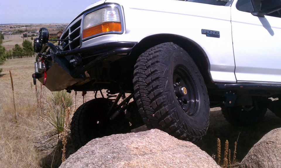Lifted white Ford Bronco XLT front corner on a boulder showing winch bumper and mud tire