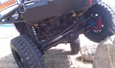 1978 Ford Bronco - The undercarriage and suspension of a modified off-road vehicle are shown in detail, with one tire on a rock.