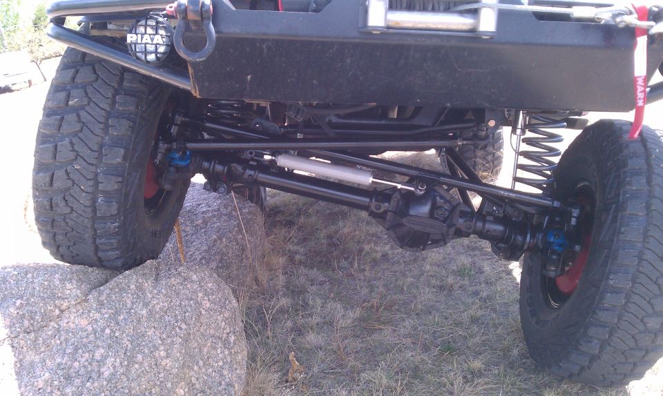 Underside of a lifted 4x4 front axle with crossover steering, coil springs, PIAA light and WARN winch