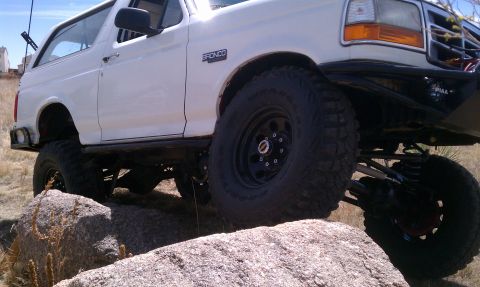 1978 Ford Bronco - This white Ford Bronco is shown navigating a rocky trail with its lifted suspension and aggressive off-road tires.