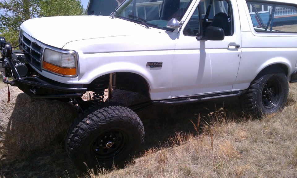Lifted white Ford Bronco with front tire climbing a boulder, showing lifted suspension