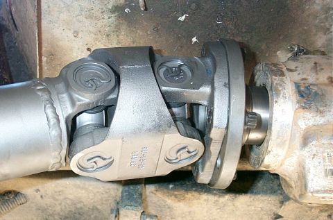 1990 Ford Bronco - Underside close-up of a driveshaft's double-cardan (CV) joint with grease-fitting-equipped Spicer u-joint caps, shown next to the splined o…