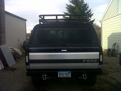 1994 Ford F-150 - This 1994 Ford F-150 pickup truck is seen from the rear, equipped with a camper shell and a roof rack.